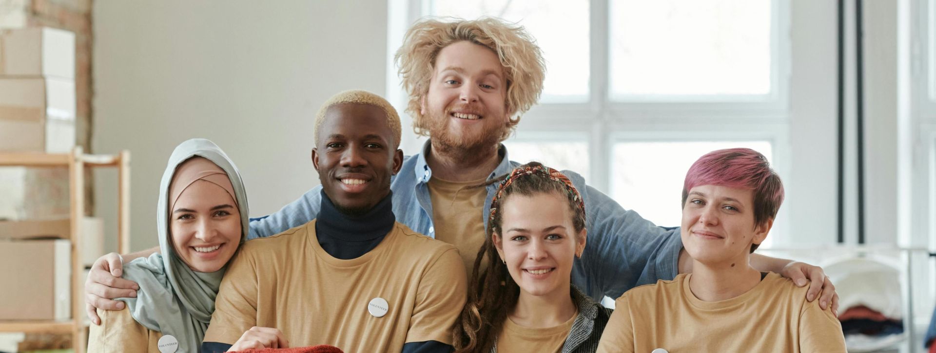 Group of diverse volunteers smiling while sorting clothes at a charity donation center.