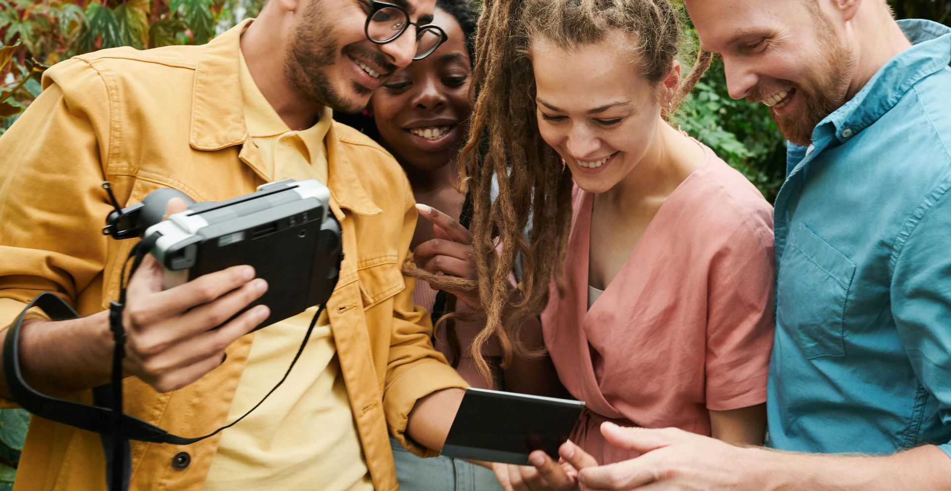 Diverse group of friends smiling and looking at photos on a camera outdoors in a garden.