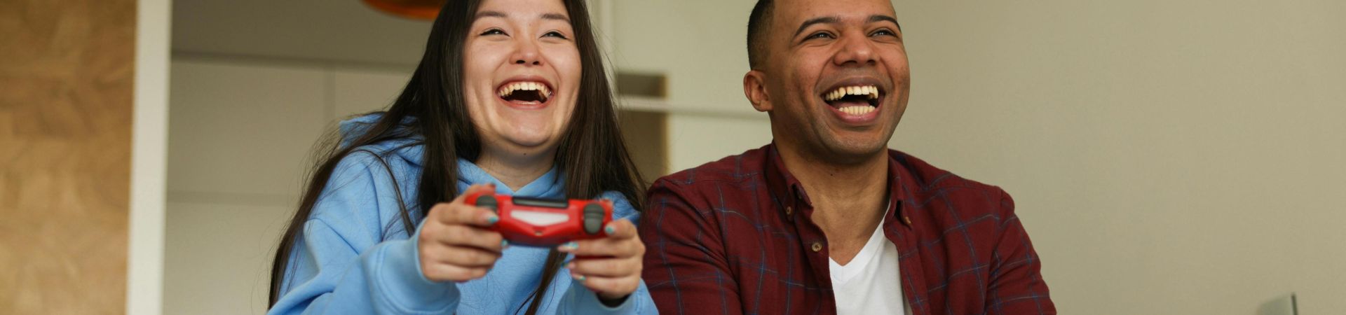 Cheerful interracial couple having fun playing video games on a sofa, showcasing happiness and technology.